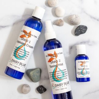 Three blue bottles of the 3 Step Face Set - Normal / Dry—Cleansing Cream, Toning Mist, and Facial Moisturizer—are displayed on white marble with small stones. "Best Seller" is shown at the top left. Ideal for dry skin.