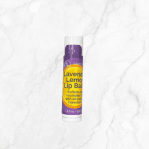 A tube of lavender lemon lip balm, featuring a purple and yellow label with all-natural ingredients (0.2 oz), stands upright on white marble—perfect to pair with your Flawless Glow Blush routine.