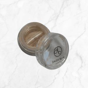 An open Flawless Glow Blush sits on a white marble surface, featuring a small clear plastic container with a transparent lid and filled with light beige powder.
