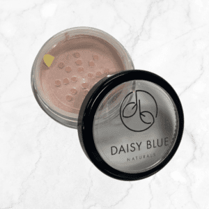 A round Flawless Glow Blush container with a black-rimmed clear lid, partially open to reveal light pink powder, sits elegantly on a white marble surface.