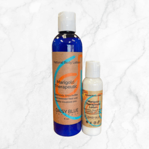 A large and a small bottle of Marigold 'Therapeutic' Hand & Body Lotion sit side by side on white marble, each with blue and white labels accented in orange and teal.