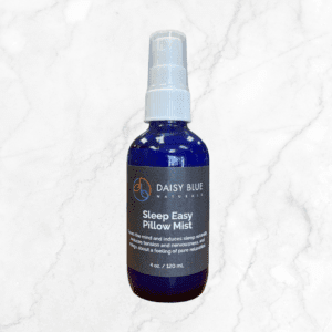 A blue spray bottle labeled "Sleep Easy Pillow Mist" rests on a white marble surface, with the label highlighting its calming properties for restful sleep and relaxation.