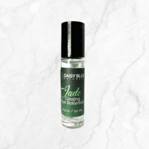 A small glass bottle of Jade Cooling Eye Rollerball sits on white marble. The green label with white text highlights the 0.3 oz (10 mL) formula inside, and the black cap completes this cooling eye product.
