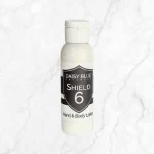 A small white bottle labeled "Shield 6 Protective Hand & Body Lotion" stands upright on a light marble background, emphasizing the gentle care this lotion brings to any skincare routine.