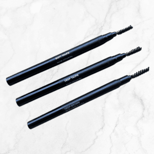 Three Retractable Brow Pencils with Spoolie Brush in the shades SOFT TAUPE, DEEP TAUPE, and DEEP BROWN are arranged diagonally on a light marble background.