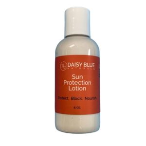 A white bottle of Daisy Blue Naturals Sun Protection Lotion with an orange label reads: "Sun Protection Lotion. Protect. Block. Nourish. 4 oz." Pair with Summer Body Oil for hydrated, sun-safe skin.