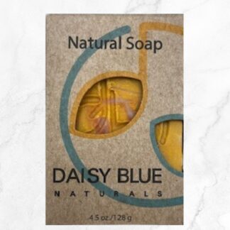 A brown paper package with a cutout displays yellow Cassia & Cedar Body Bar Soap inside. The label reads "Natural Soap" and "DAISY BLUE NATURALS, 4.5 oz/128g" with a blue and gold design.