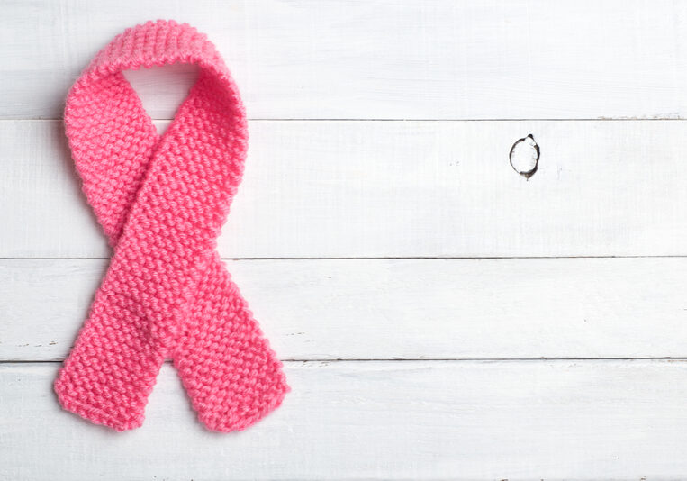 A pink knitted ribbon in the shape of a loop, symbolizing breast cancer awareness and honoring cancer survivors, placed on a white wooden background.