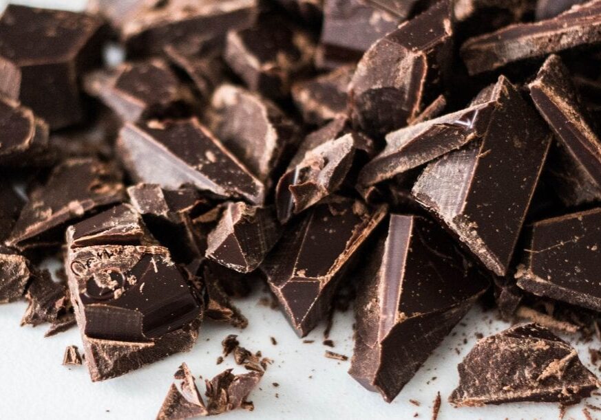 Chunks of broken dark chocolate scattered on a white surface. The chocolate pieces are of various shapes and sizes, with rough edges and a rich, glossy appearance—perfect for exploring fascinating Top Chocolate Facts.