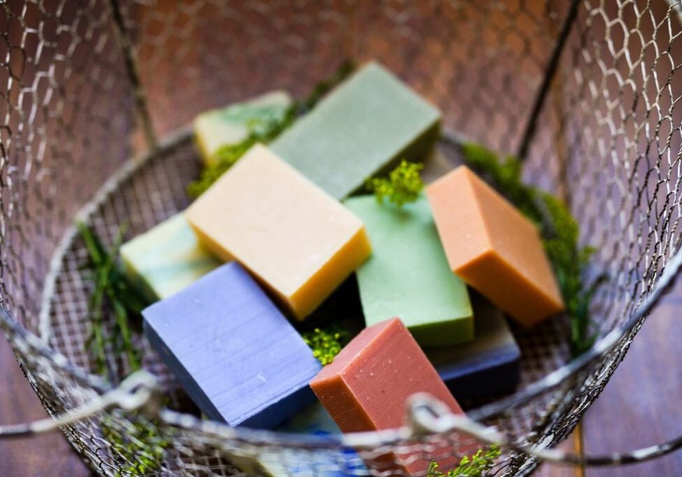 A wire basket filled with assorted bar soap in shades of purple, green, orange, yellow, and beige sits among bits of greenery—a Treehugger’s dream collection that makes choosing just one a delightful slippery slope.